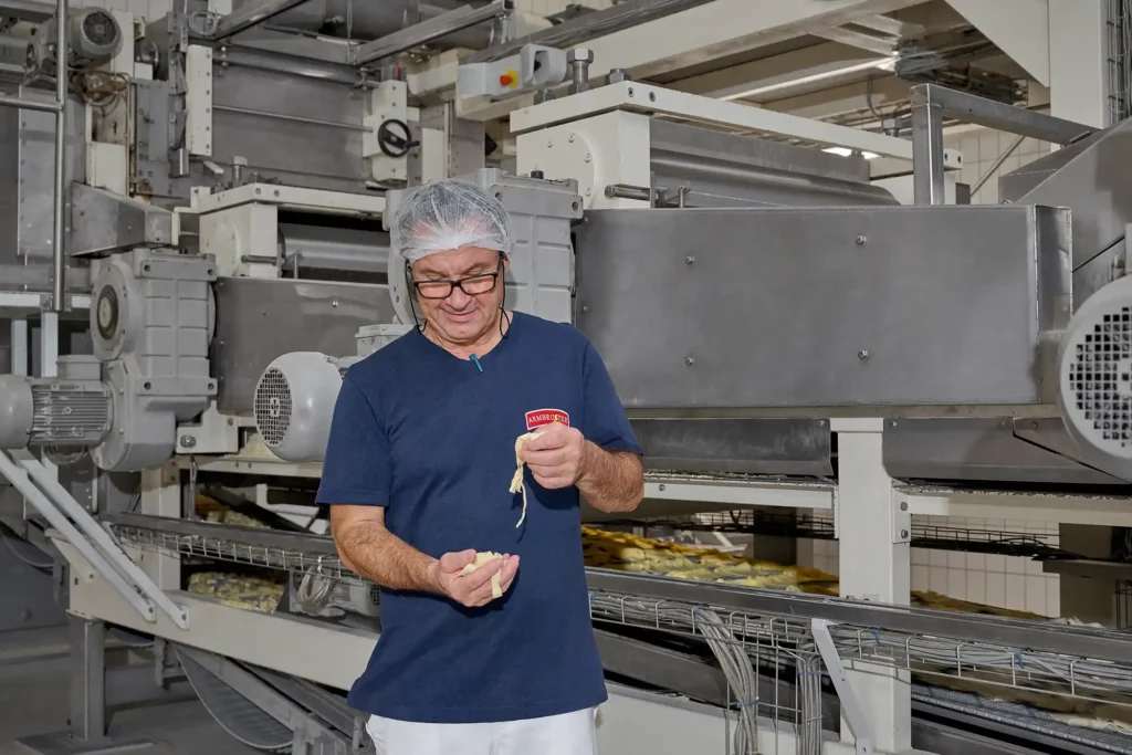 Mitarbeiter im Werk hällt Nudel in der Hand